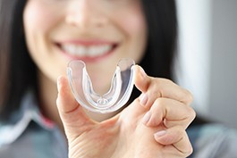 Woman smiling while holding clear mouthguard