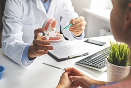 Dentist’s hands showing model teeth to patient during discussion