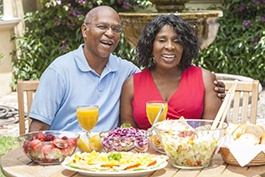 couple sitting at a table outside with various foods and drinks
