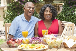 couple sitting at a table outside with various foods and drinks 