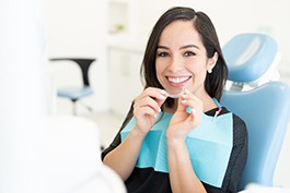 Woman smiling in treatment chair while holding clear aligner