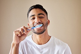 Man in white shirt smiling while brushing his teeth