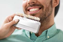 a dentist matching the color of a patients’ teeth to a shade chart