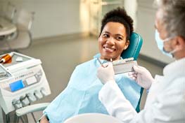 a dentist holding a shade chart in front of a patient’s teeth while they sit in a treatment chair