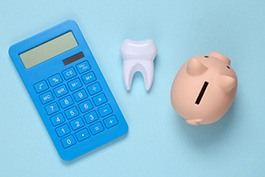 A calculator, tooth model, and piggy bank against a blue background