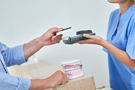 A partially-visible patient paying the cost of veneers