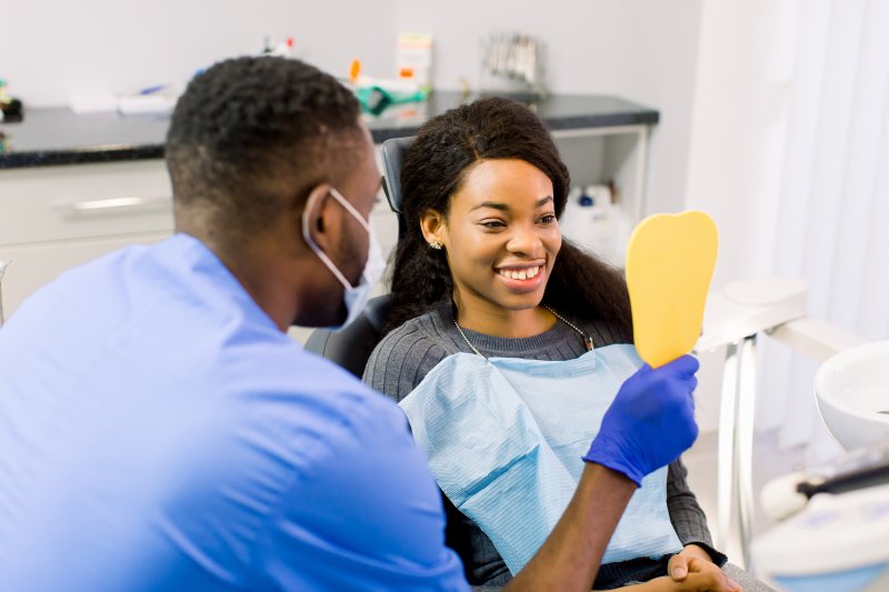 a young woman smiling at herself while the dentist holds the mirror 