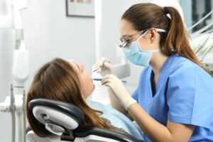 Dental hygienist in blue scrubs examining patient's mouth