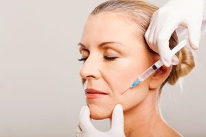 3/4 profile view of woman with hair in a bun getting Botox injection in lip area